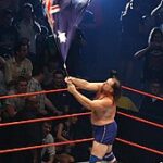 Duggan waving an Australian flag during his ring entrance in Australia, 2007, with his 2x4 in the corner